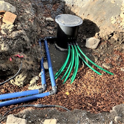 Obr. Nejvzdálenější šachta Š1, na kterou jsou napojeny 4 vrty (zelená potrubí) a společné páteřní potrubí (modré) směřující k šachtě Š2. (Foto: Fránek, léto 2018)